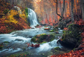 Afwasbaar Fotobehang Watervallen Prachtige waterval bij bergrivier in kleurrijk herfstbos met rode en oranje bladeren bij zonsondergang. Natuur landschap
