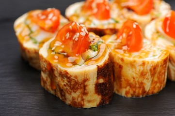 Set of fusion japanese rolls with omelette and tomatoes on black