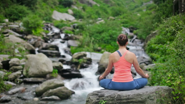 Woman meditating at tropical waterfall