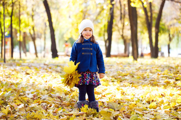 little girl keeps leafs in hand in park in the autumn