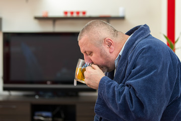 Ill man blowing his nose with paper napkin and drinking tea at home