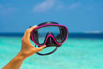 hands holding scuba mask on tropical beach