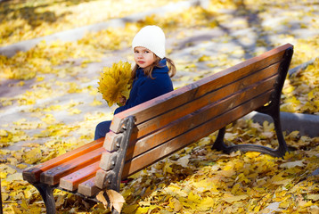 Little girl sitting on a bench in the park