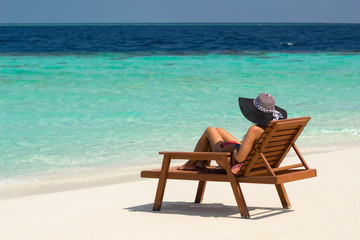 Fototapeta na wymiar Young woman sunbathing on lounger at tropical beach