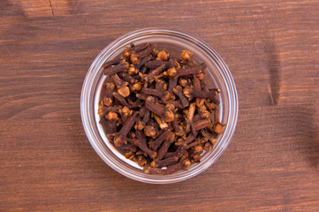 Cloves on bowl on wooden table seen from above