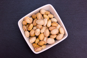 Pistachios on a square bowl on slate top seen from above