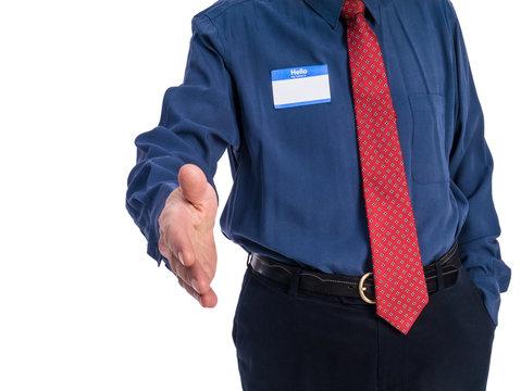 Photo of senior man in a blue shirt and red tie wearing a "Hello My Name Is" name tag. He is extending his hand in greeting.