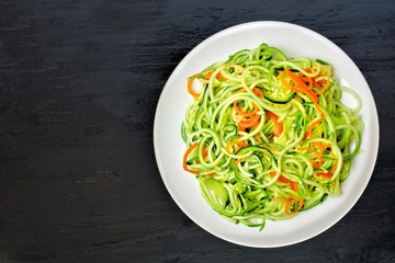 Low carb zucchini noodle dish with carrots and lime on dark slate background, overhead view