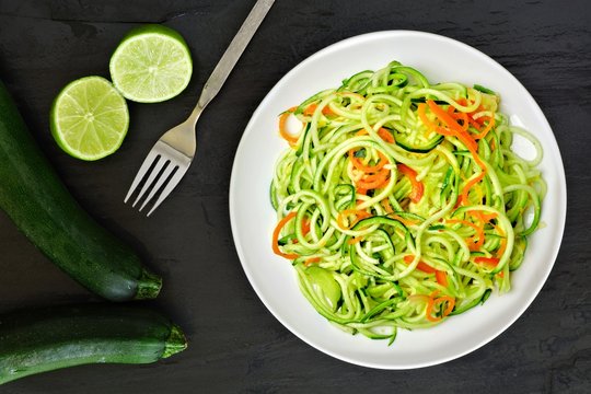 Healthy zucchini noodle dish with carrots and lime on dark slate background, overhead view