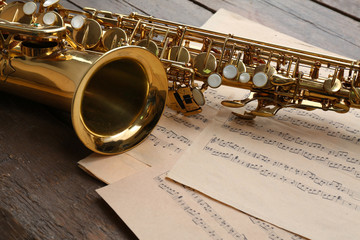 Beautiful golden saxophone with musical notes on wooden background, close up - obrazy, fototapety, plakaty