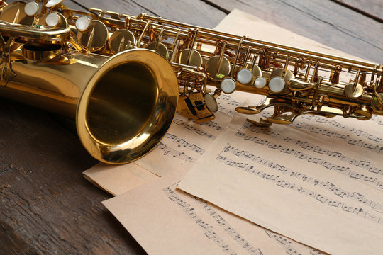 Beautiful golden saxophone with musical notes on wooden background, close up