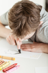 Serious Boy Coloring his Drawing on a White Paper