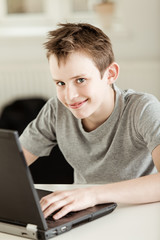 Happy young schoolboy working on a laptop