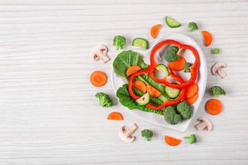 Useful cut vegetables on a plate in the form of heart on wooden table top view