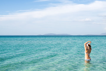 Back of beautiful woman wearing blue bikini standing in the water on Mediterranean sea coast, Cesme, Ilica beach, Turkey. 