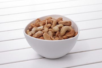 Pile of cashew nuts in a bowl on white wooden table