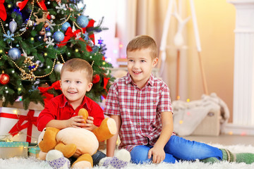Two cute small brothers with teddy bear on Christmas tree background