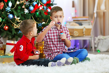 Two cute small brothers blows soap bubbles on Christmas tree background