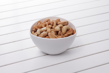 Pile of cashew nuts in a bowl on white wooden table
