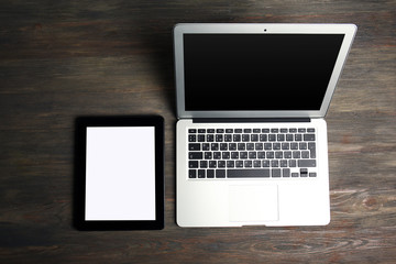 An open silver laptop and modern tablet on the wooden background