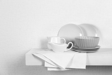 Set of tableware with napkin on shelf against white wall background