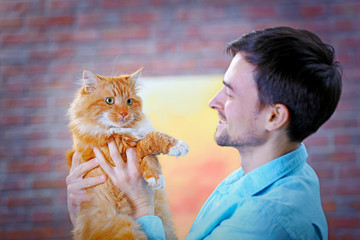 Smiling young man holding a fluffy red cat