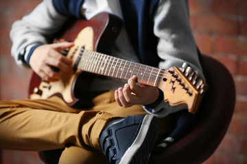 Fototapeta na wymiar Cute little boy playing guitar on brick wall background