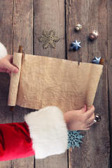 A list of Christmas wishes in Santa Claus hands on wooden background