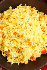Stewed rice with a carrot on a black plate, close up