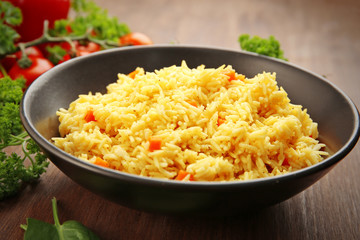 Stewed rice with a carrot on a black plate over wooden background, close up