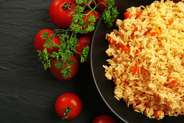 Stewed rice with a carrot and tomatoes on a plate over black background, close up