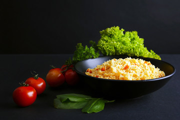 Stewed rice with a carrot and tomatoes on a plate over black background