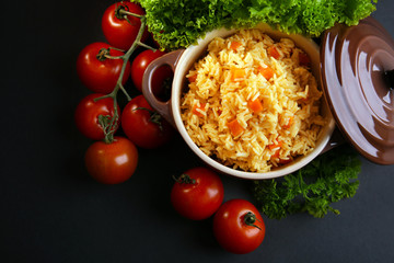 Stewed rice with a carrot and tomatoes in a cooking pot over black background, close up