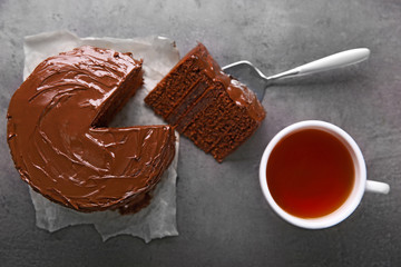 Chocolate cake with a cut piece and blade and cup of tea on gray background, closeup