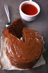 Chocolate cake with a cut piece and blade and cup of tea on gray background, closeup
