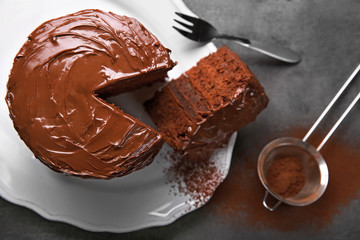 Chocolate cake on plate with a cut piece and fork and cocoa on gray background, closeup