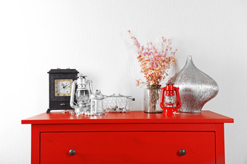 Room interior with red wooden commode, lanterns and clock on light wall background
