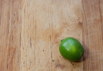 Lime situated on bottom right corner of well-worn butcher block with wood planks in vertical  pattern