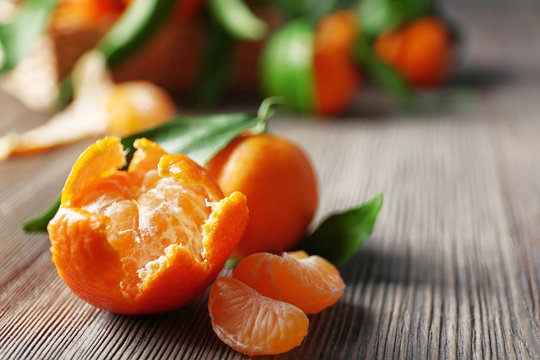 Peeled fresh tangerine with leaves and ripe mandarins on wooden table, closeup