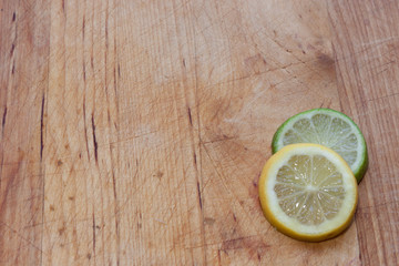 Lemon and lime round slices on bottom right corner of well-worn butcher block with wood planks in vertical pattern