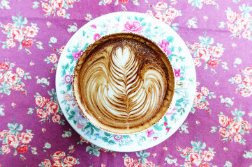 cup of latte art coffee on background texture fabric floral pattern.