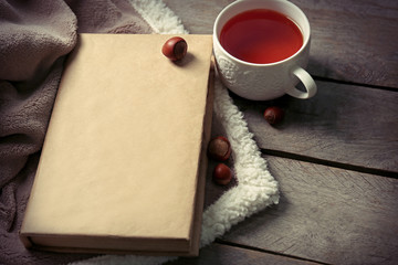 A book, a cup of tea, a hazelnut and a blanket on the wooden background