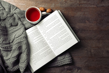 An open book, a cup of tea and a blanket on the wooden background