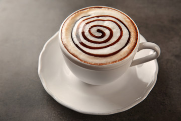 Cup of hot cappuccino with chocolate syrup on grey table
