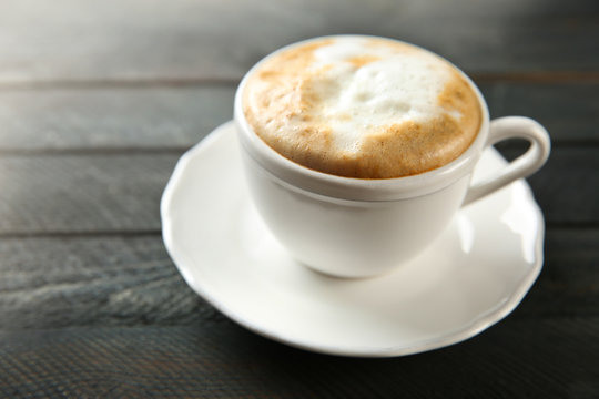 Cup of hot cappuccino with froth on a black wooden table