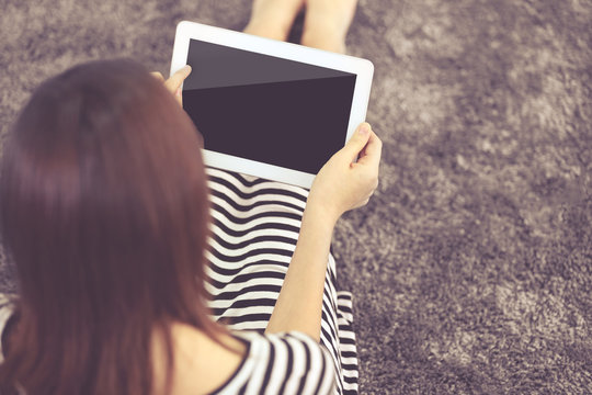 Girl With Digital Tablet On Carpet Indoor, Back View