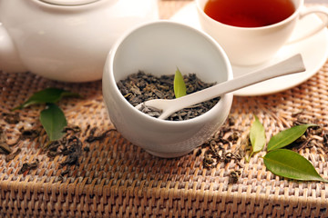 Granulated tea with green leaves in tea-set on wicker tray closeup