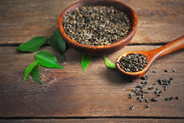 Granulated tea with green leaves in wooden bowl on table closeup