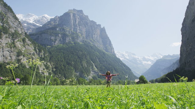 Woman dancing having fun in happy grass field in Switzerland Swiss Alps. Girl laughing swirling around in Lauterbrunnen valley with Jungfrau, Eiger and Monch mountains in background. RED EPIC Footage.