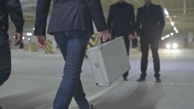 Two criminals walking towards their partners and opening metal briefcase in front of them